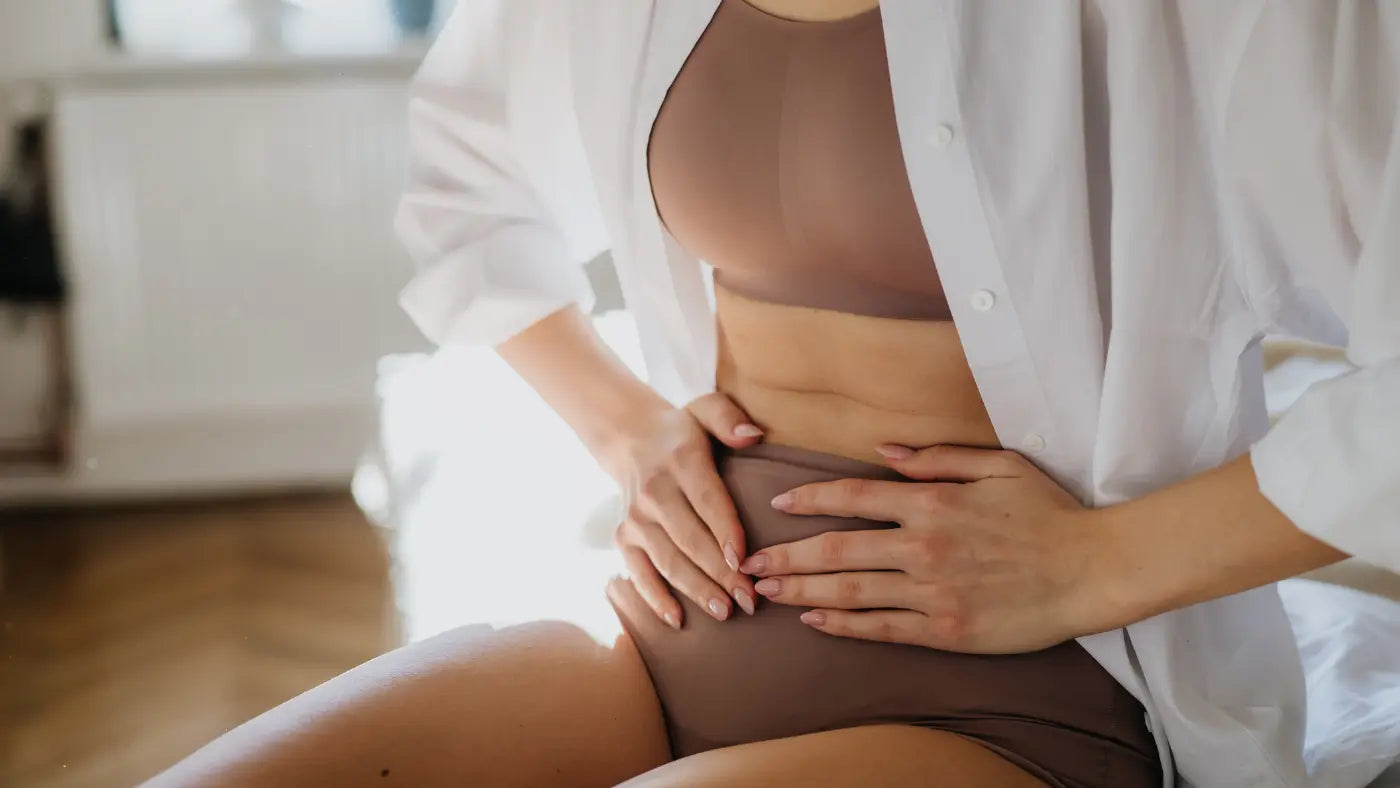 Frau hält mit beiden Händen ihren aufgeblähten Bauch