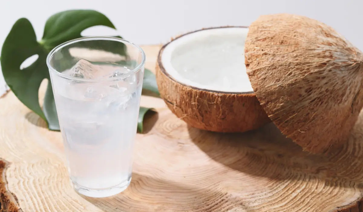 Kokoswasser in einem Glas neben einer Kokosnuss