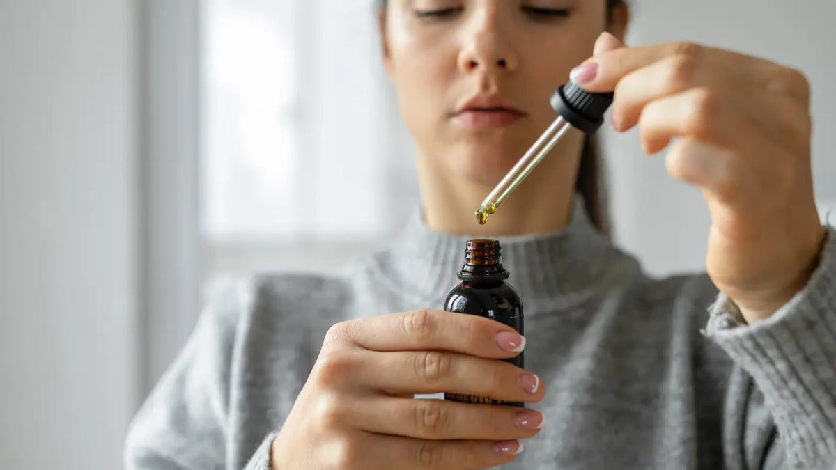 Frau im grauen Pullover hält CBD-Öl mit Pipette