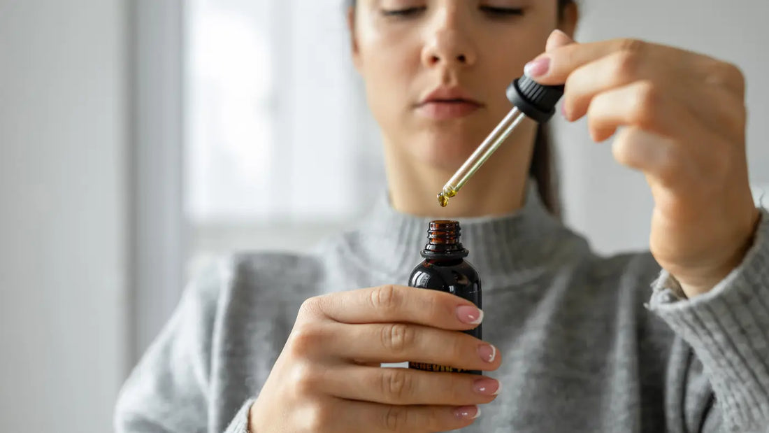 Frau im grauen Pullover hält CBD-Öl mit Pipette