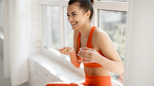 Frau in orange-farbener Sportkleidung, die glücklich das Nahrungsergänzungsmittel in der Hand hält.